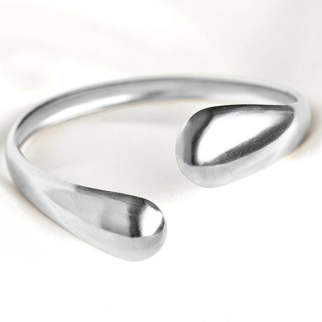 A polished silver open cuff bracelet with a smooth, organic teardrop-shaped end, photographed on a clean white background.