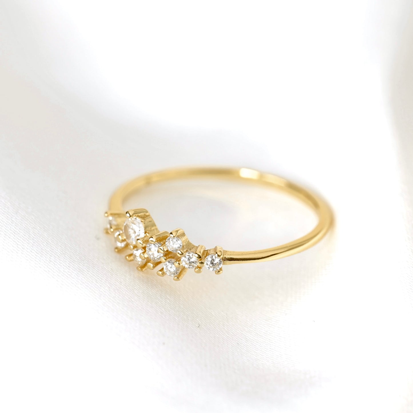 A delicate yellow gold ring featuring a small cluster of clear round-cut and marquise-cut gemstones, displayed on a soft white fabric background.