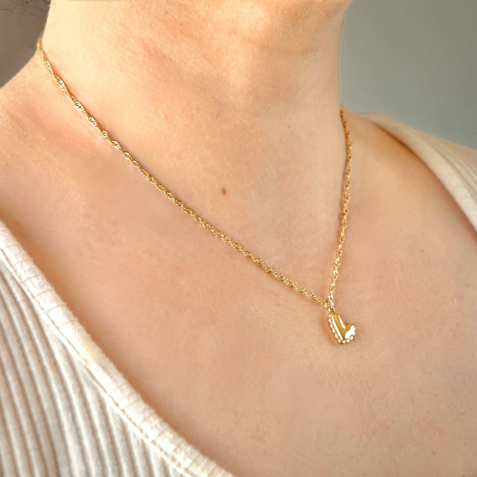 Gold singapore chain necklace with a small heart pendant on a person wearing a white top.