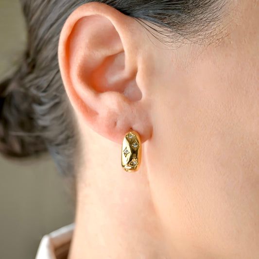 Thick Gold C hoop earrings with star set crystals worn by a person with a neutral background