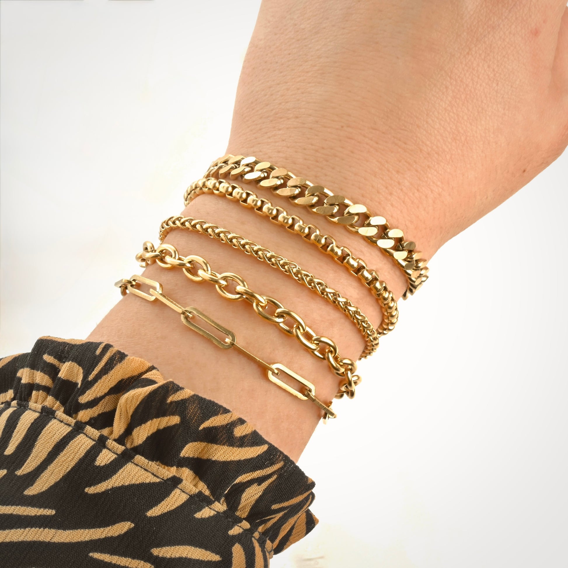 Thick Gold chain bracelets on a wrist with leopard patterned garment