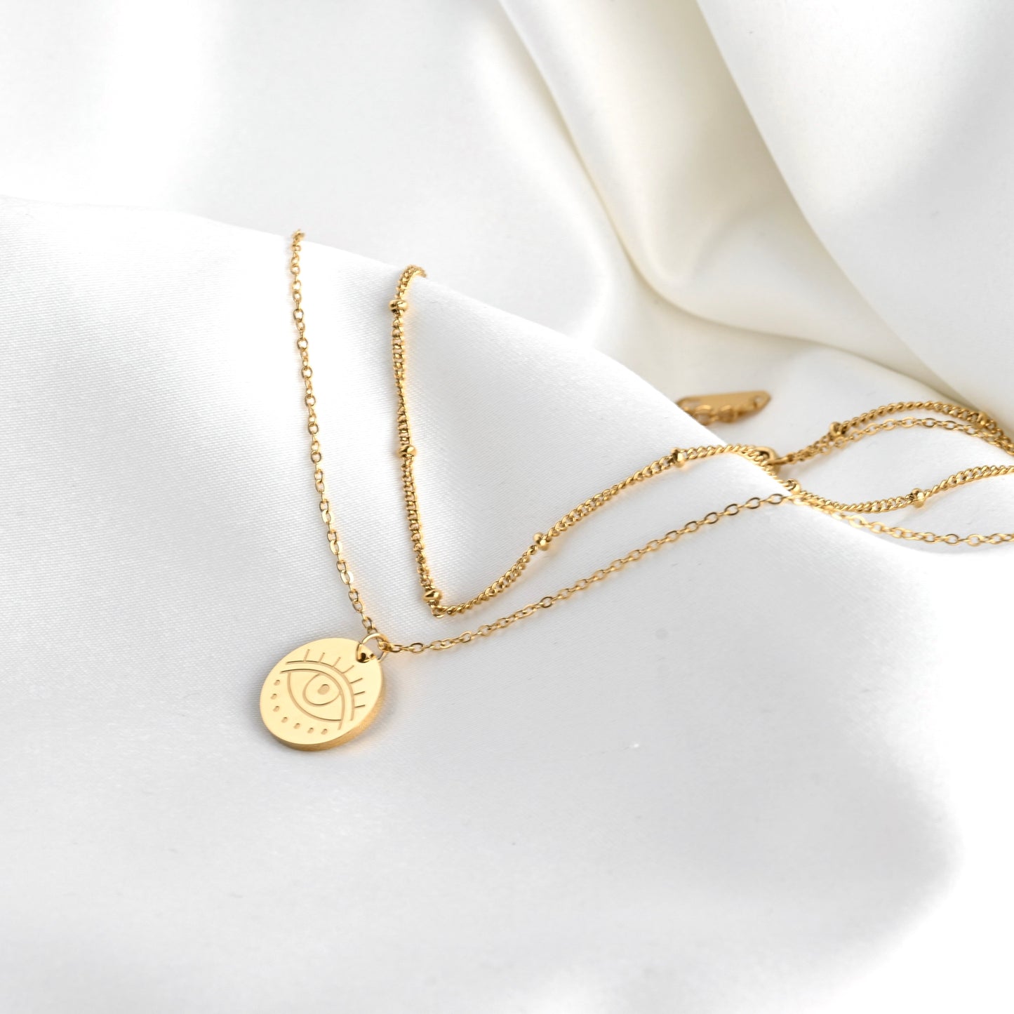 Gold necklace set with a round evil eye pendant on a white fabric background