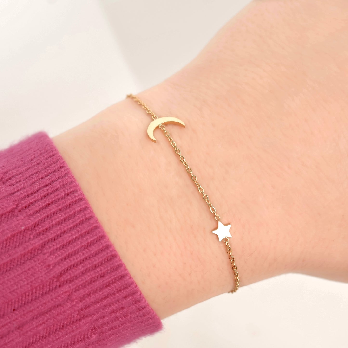 Gold crescent moon and star bracelet on a wrist wearing a pink sleeve.