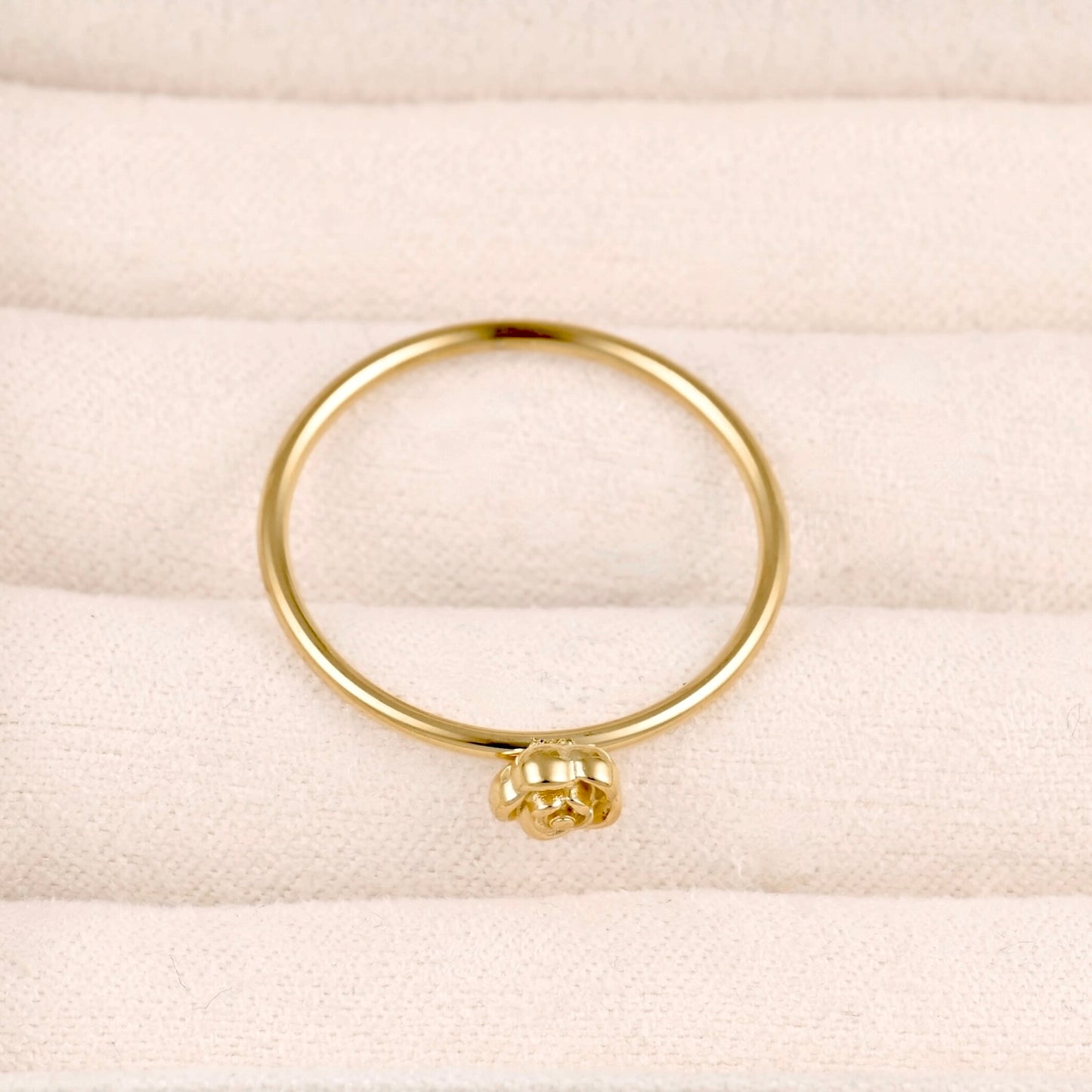 A thin yellow gold ring with a small textured flower-shaped accent at the bottom, displayed on a cream-colored textured fabric surface.