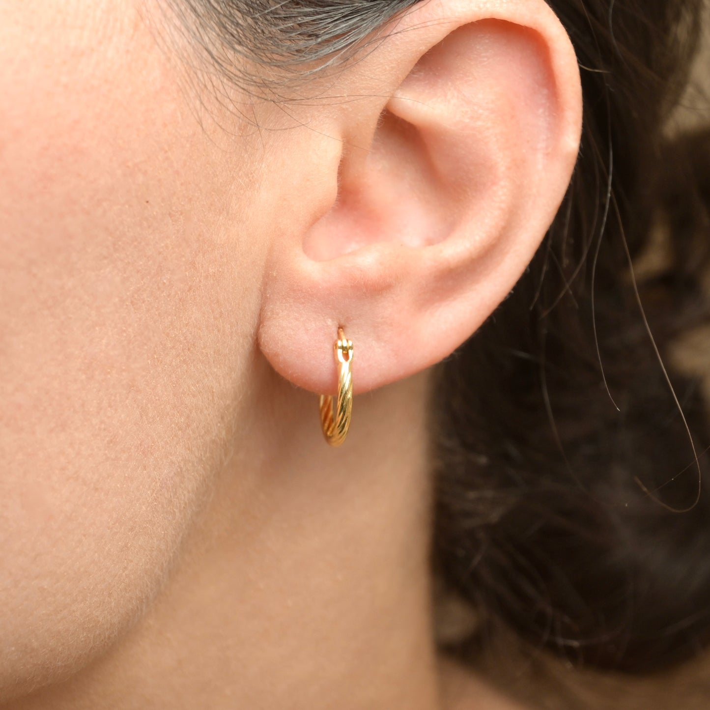 Gold hoop earring worn by a person with a neutral background