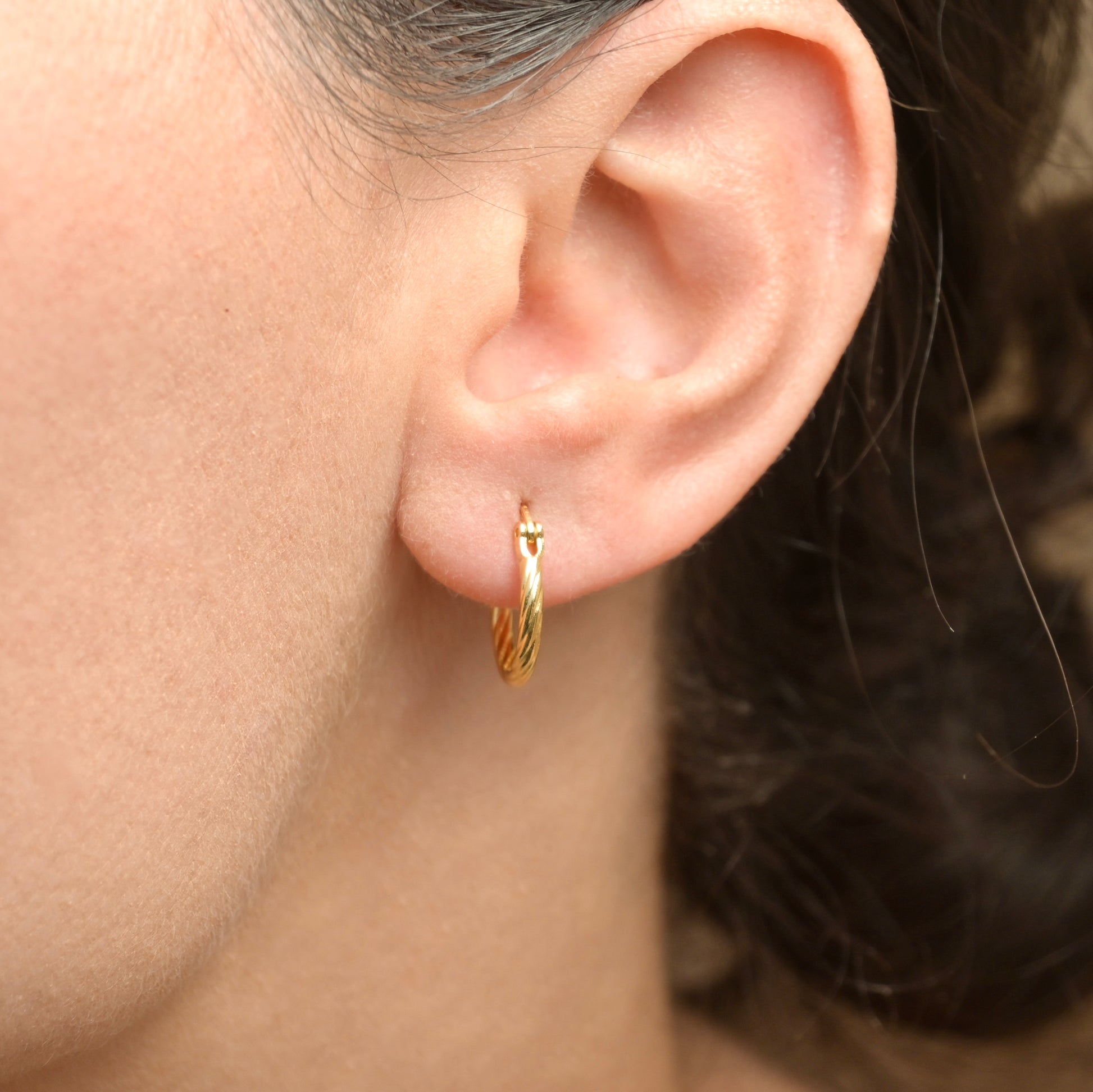 Gold hoop earring worn by a person with a neutral background