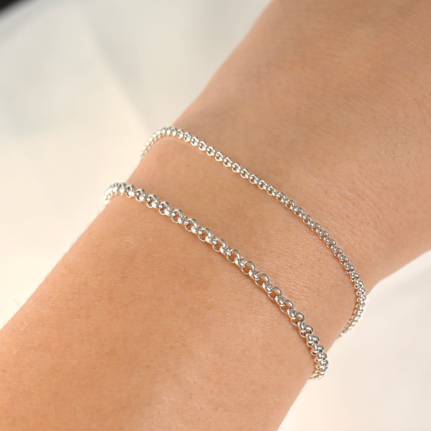 Silver chain bracelets in two widths on a wrist against a neutral background