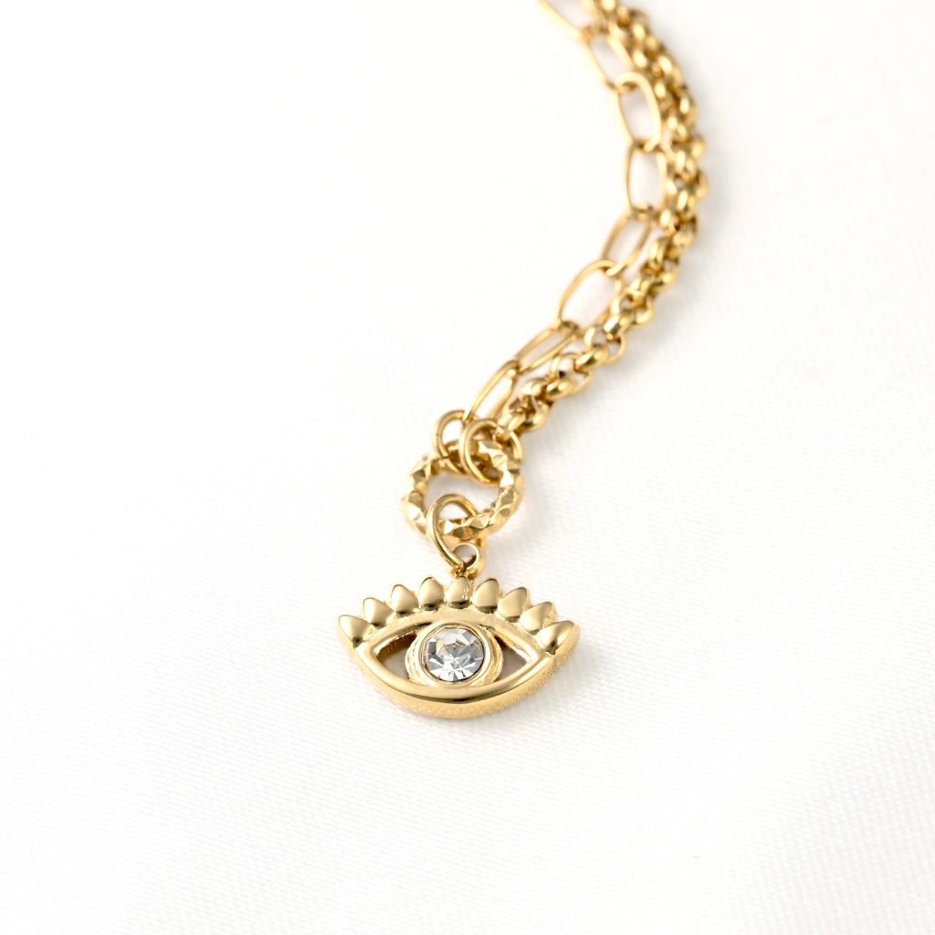 A gold-toned chain necklace featuring a stylized eye charm with a clear rhinestone in the center, displayed on a clean white background.