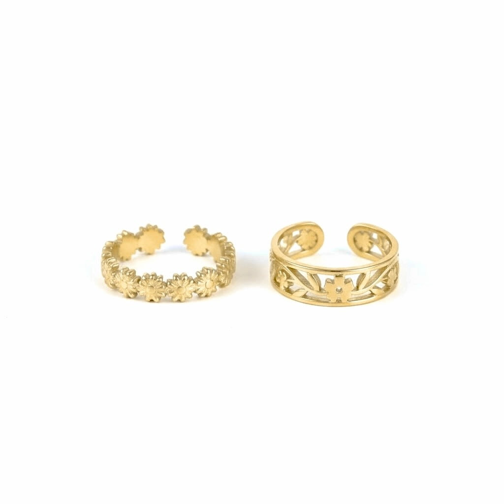 Two gold-toned open cuff rings with floral and filigree cutout details, displayed side by side on a plain white background.