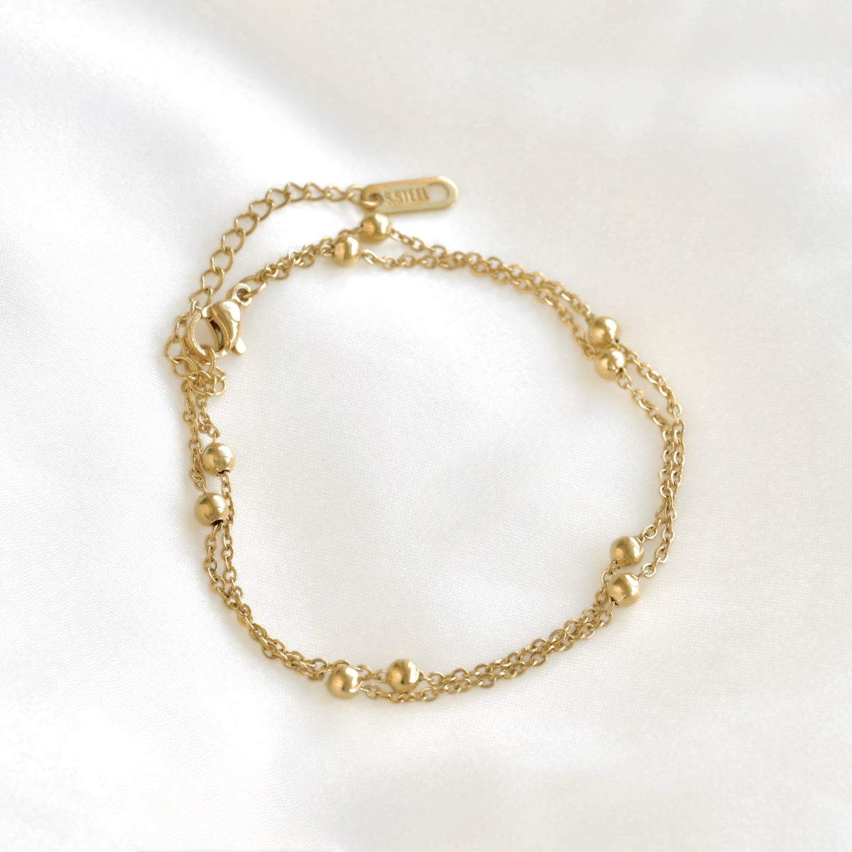 A double strand gold satellite chain bracelet with small polished bead accents and an adjustable lobster clasp, displayed on a clean white background.