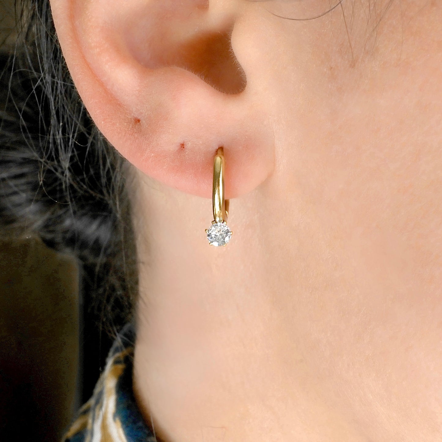 Close-up view of gold hoop earrings with a diamond on an ear