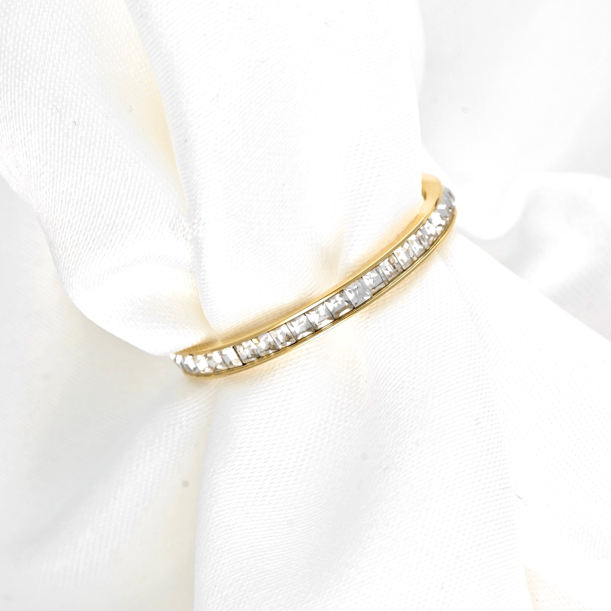 A yellow gold eternity ring with a row of clear square-cut stones, displayed on a soft white fabric napkin.