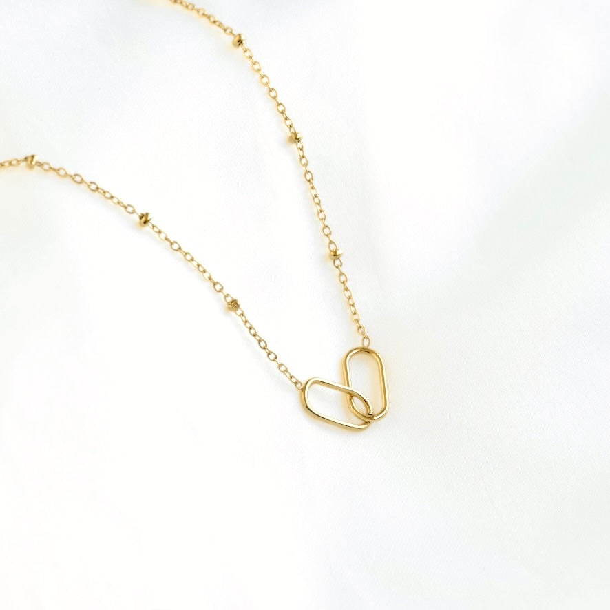 A delicate gold chain necklace featuring two interlocking open-link oval pendants, displayed on a clean white background.