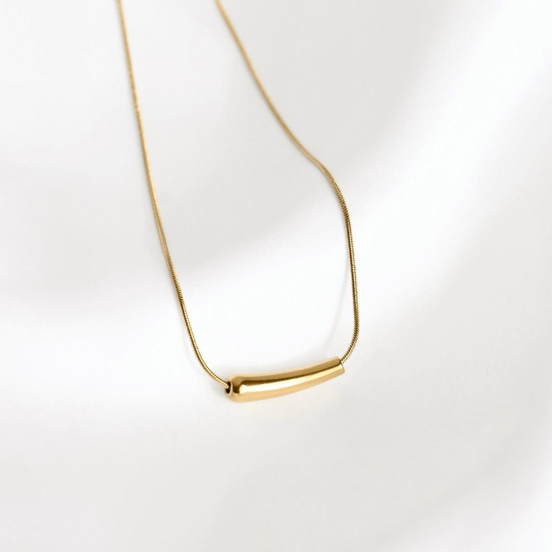 A delicate gold chain necklace featuring a small, polished horizontal bar pendant, displayed on a clean white background with soft shadows.
