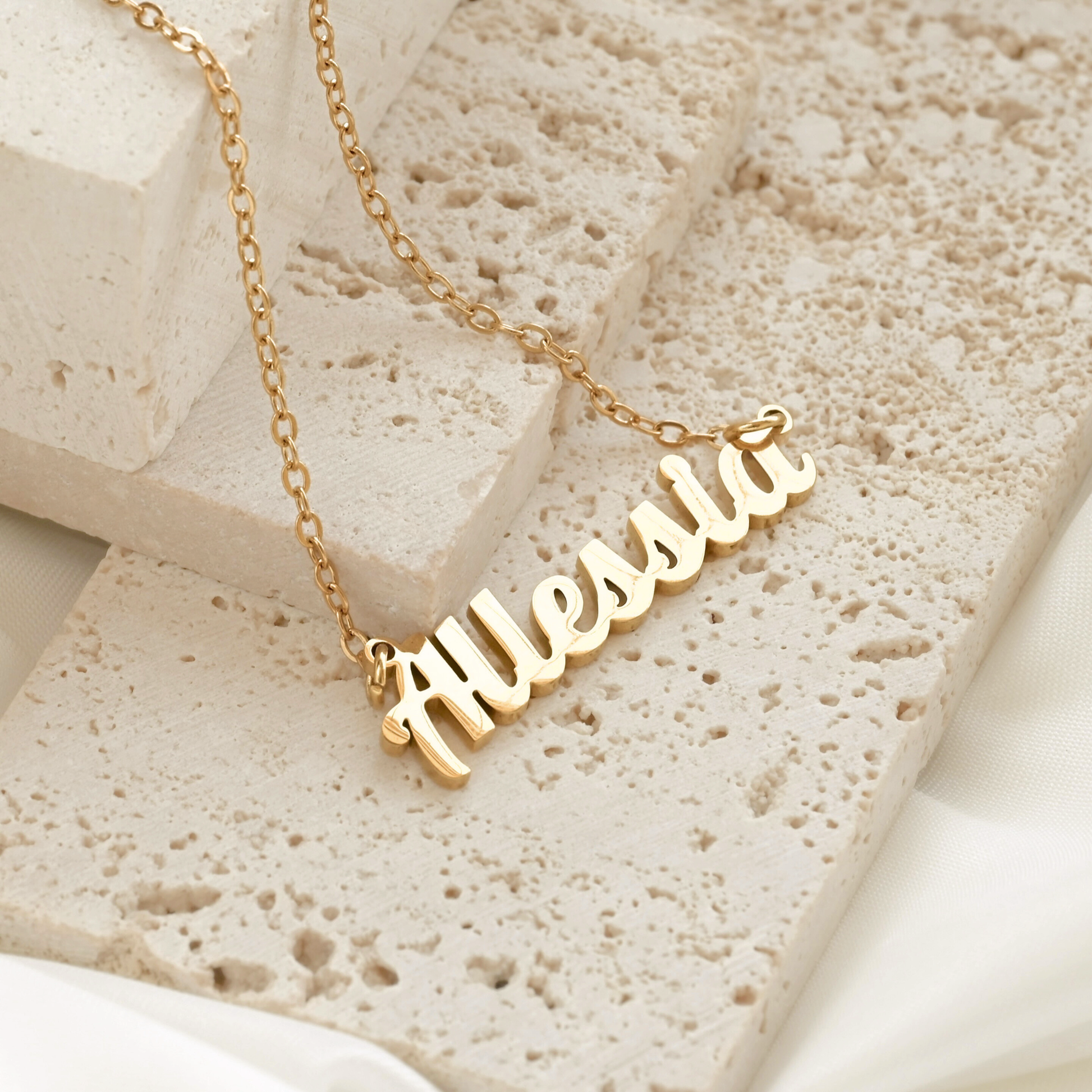 Gold necklace with 'Allessia' pendant on a textured stone surface