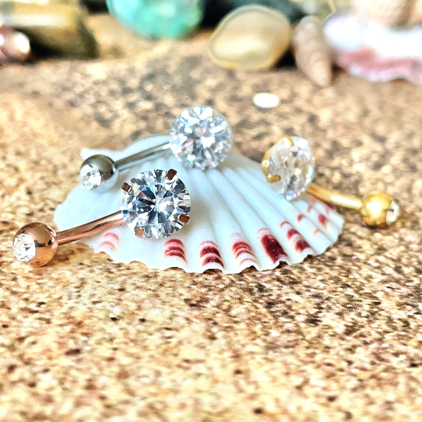 Three belly rings  with gemstones on a seashell against a textured background