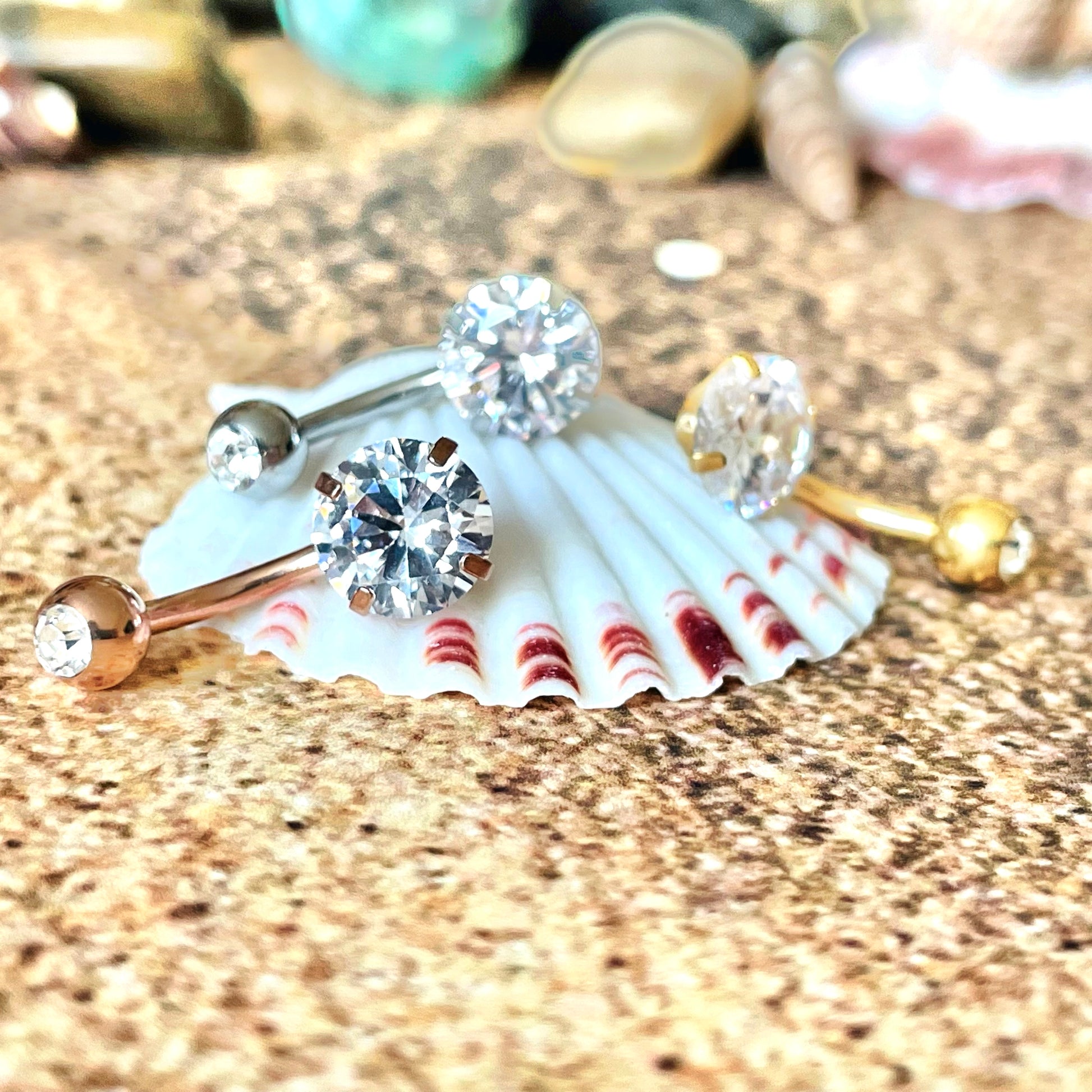 Three belly rings  with gemstones on a seashell against a textured background
