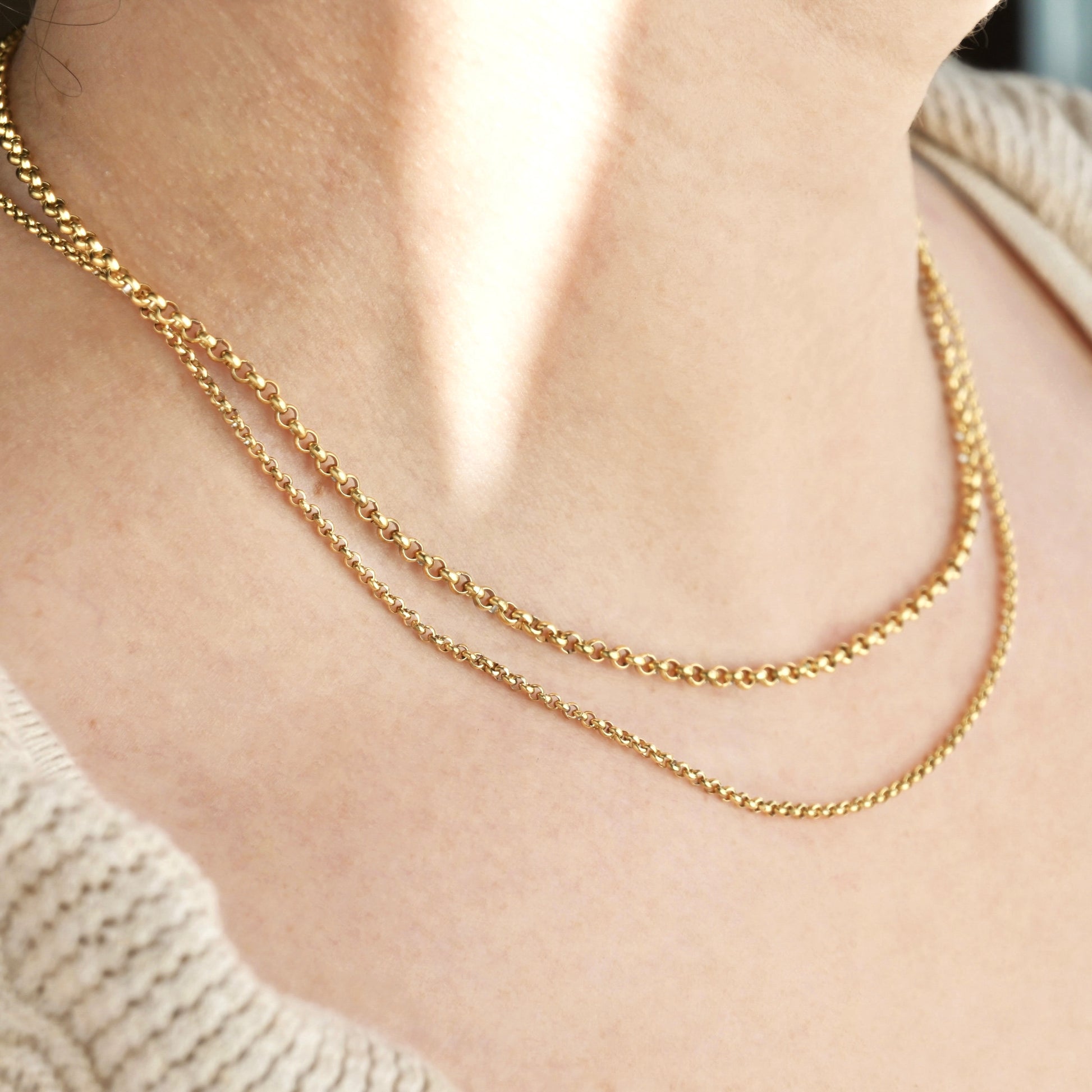 Two gold rolo chain necklace stack with 2mm and 3mm width-chains on a person wearing a beige sweater.