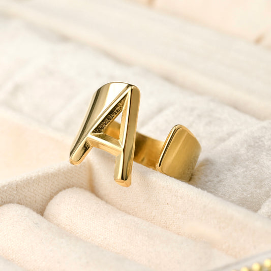 Gold letter 'A' ring on a beige cushioned jewelry box