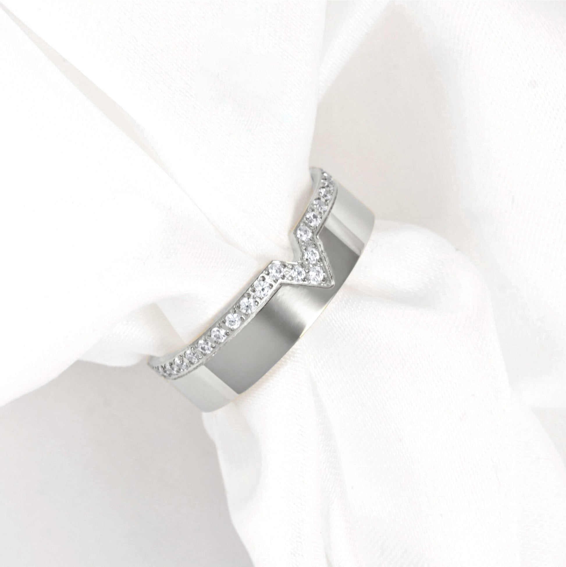 A wide silver band ring featuring a V-shaped design paved with small clear stones, displayed on a white fabric ring holder.