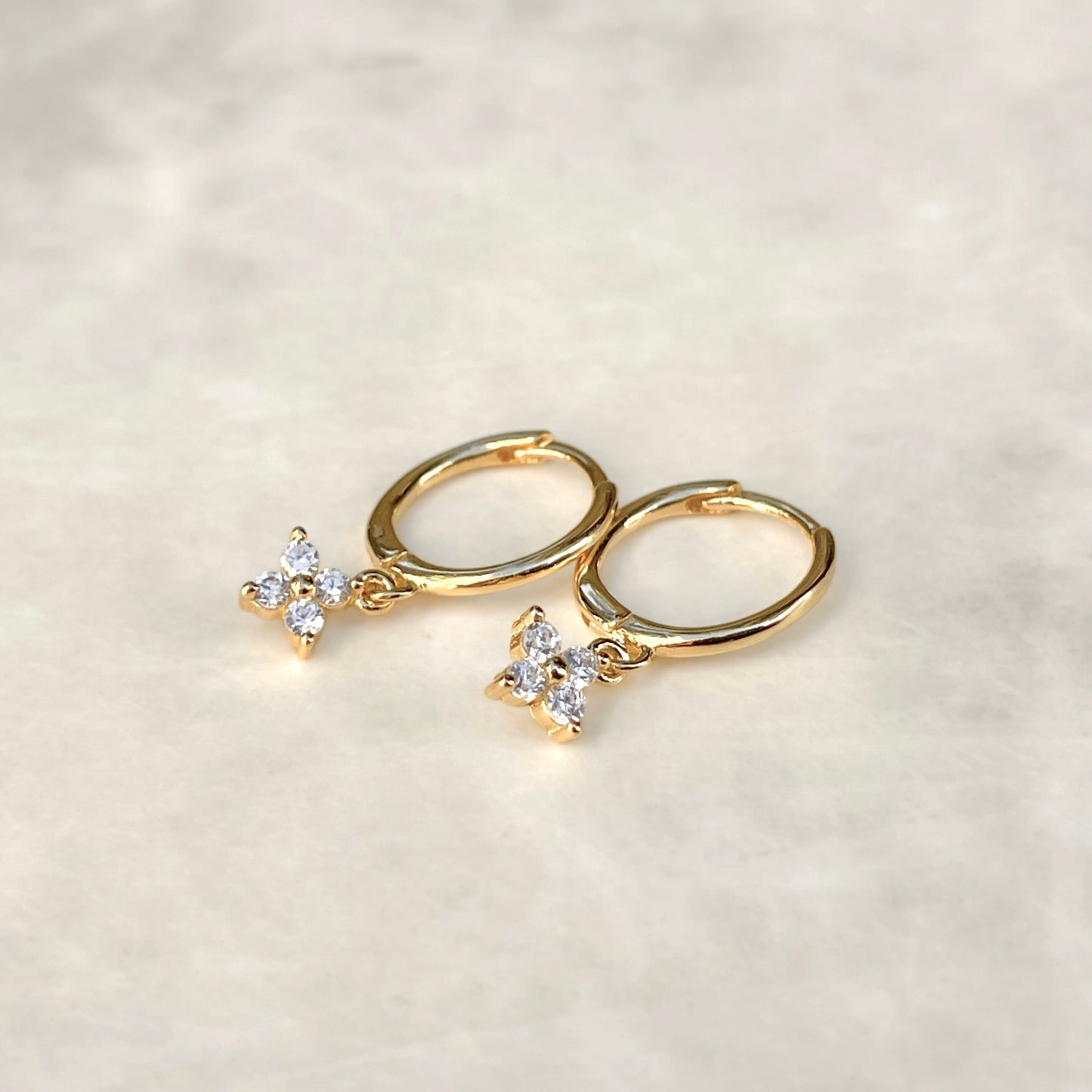 Gold hoop earrings with flower-shaped charms on a light gray background