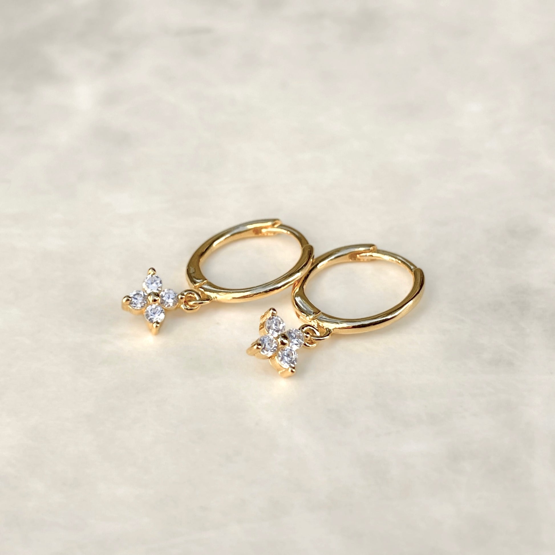 Gold hoop earrings with flower-shaped charms on a light gray background
