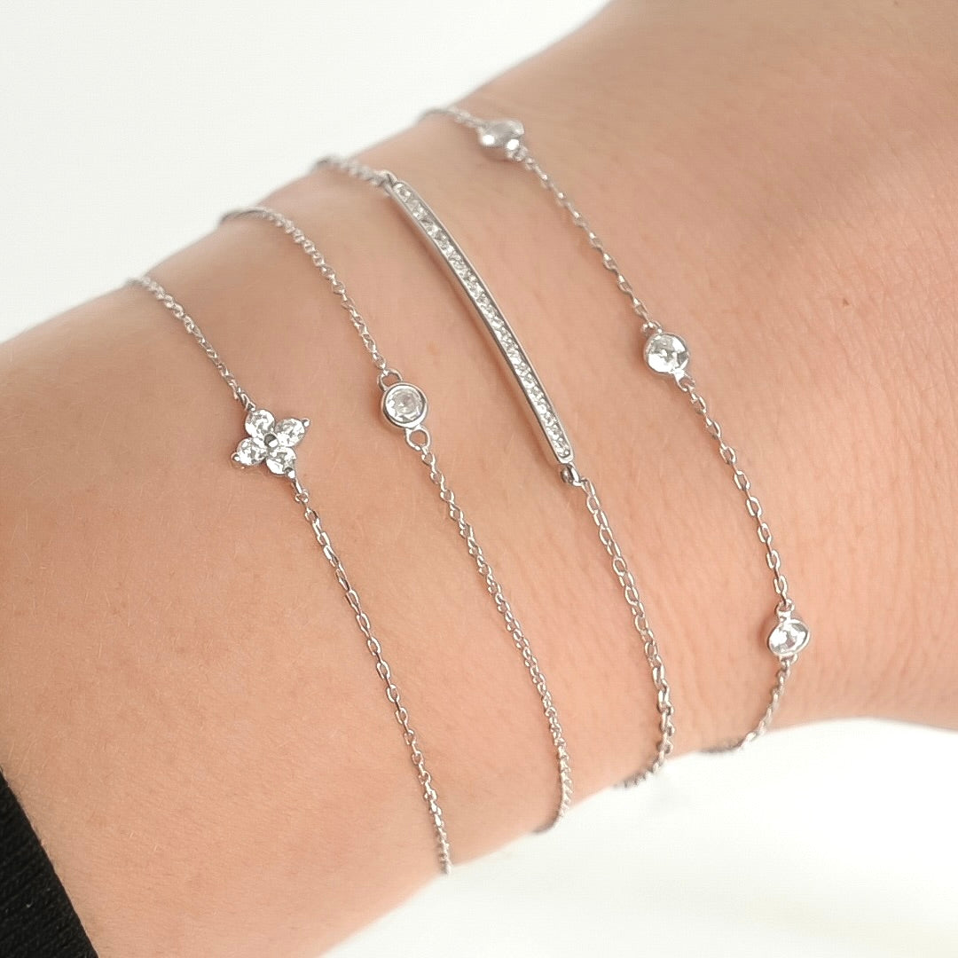 Layered silver diamond bracelets with  stone charms in various settings on a wrist against a white background