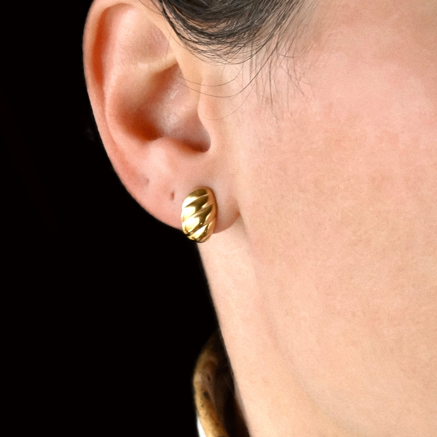 Ribbed Gold huggie earring worn on a person's ear against a black background