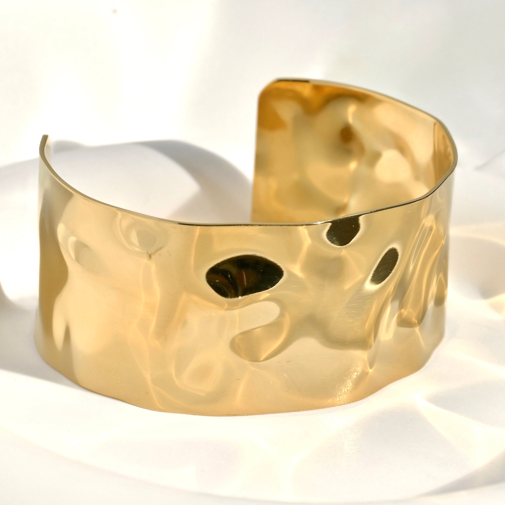Chunky gold cuff bracelet on a white background under direct sunlight