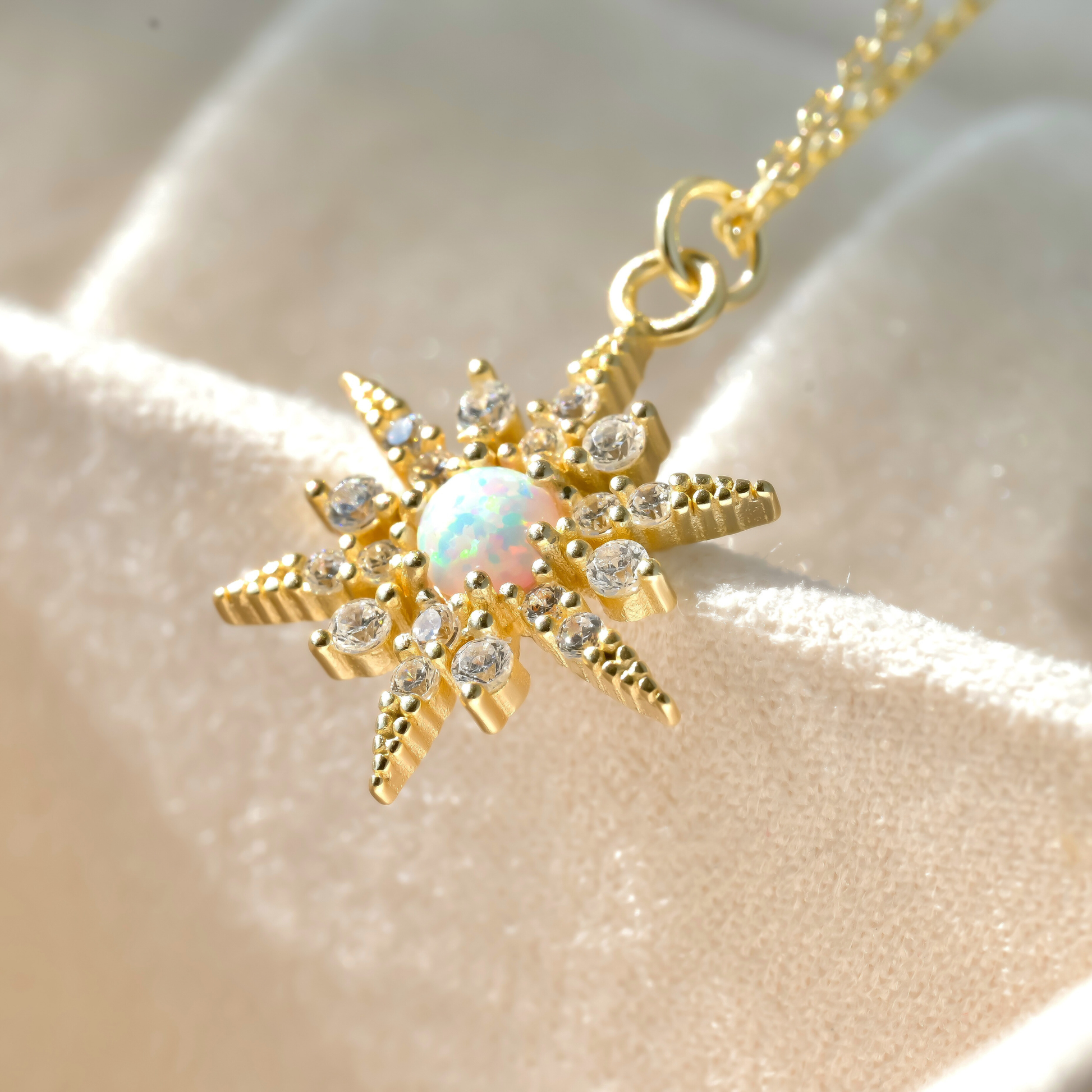 Close-up of star charm necklace with a central opal stone sparkling under direct sunlight on a beige fabric background