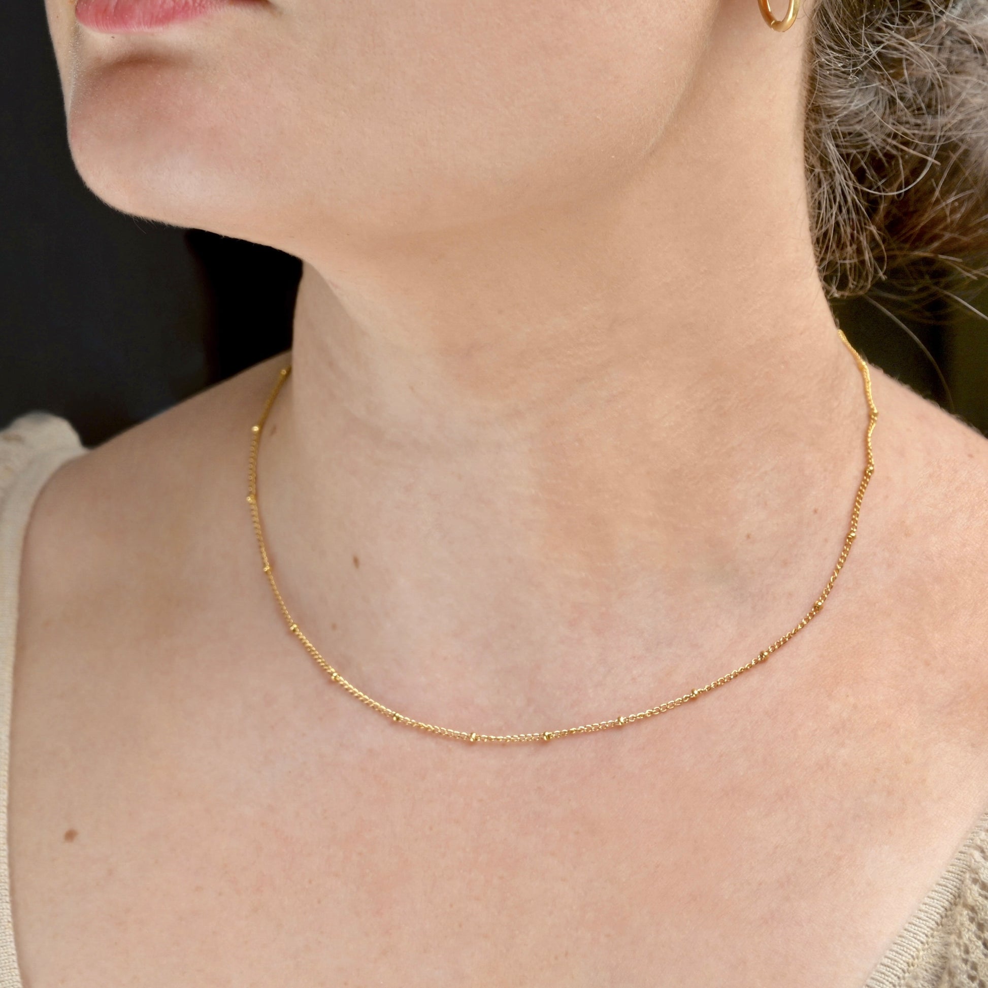 Close-up of a person wearing a gold satellite chain necklace with a blurred background