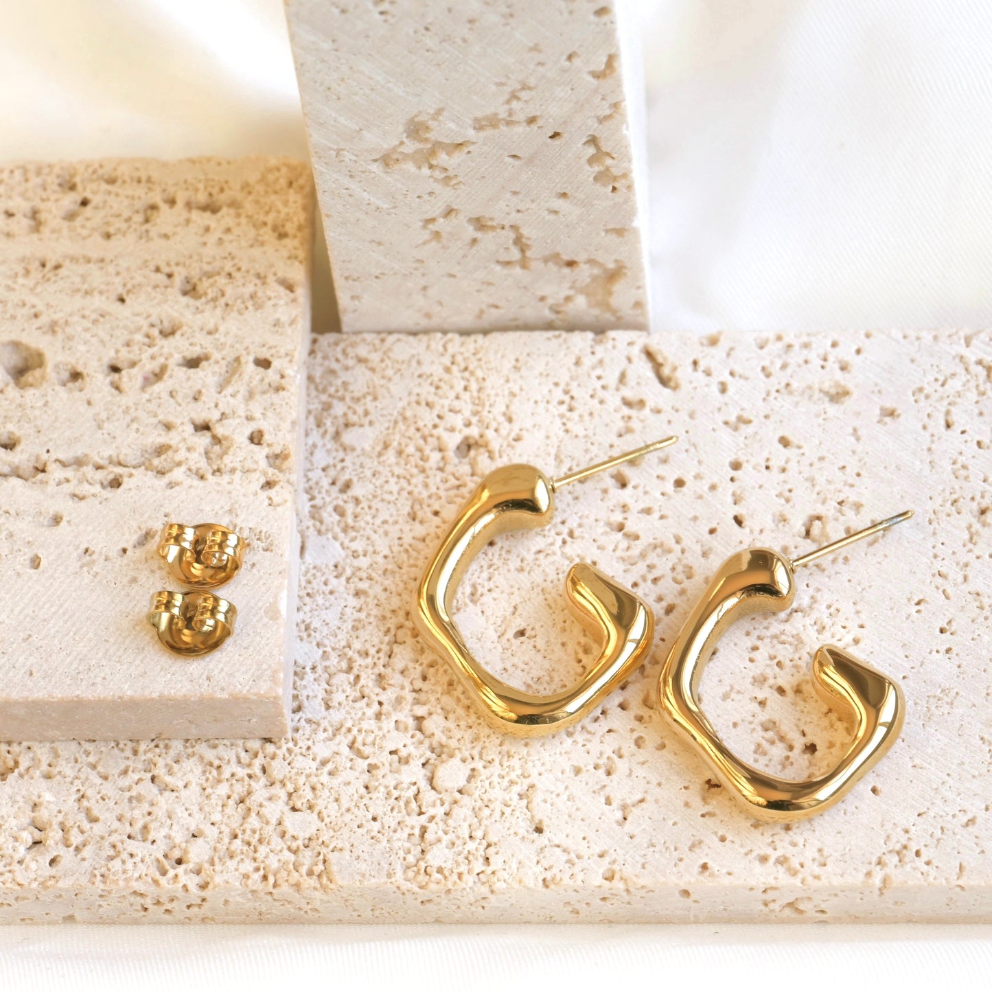 Geometric gold hoop earrings on a textured beige surface