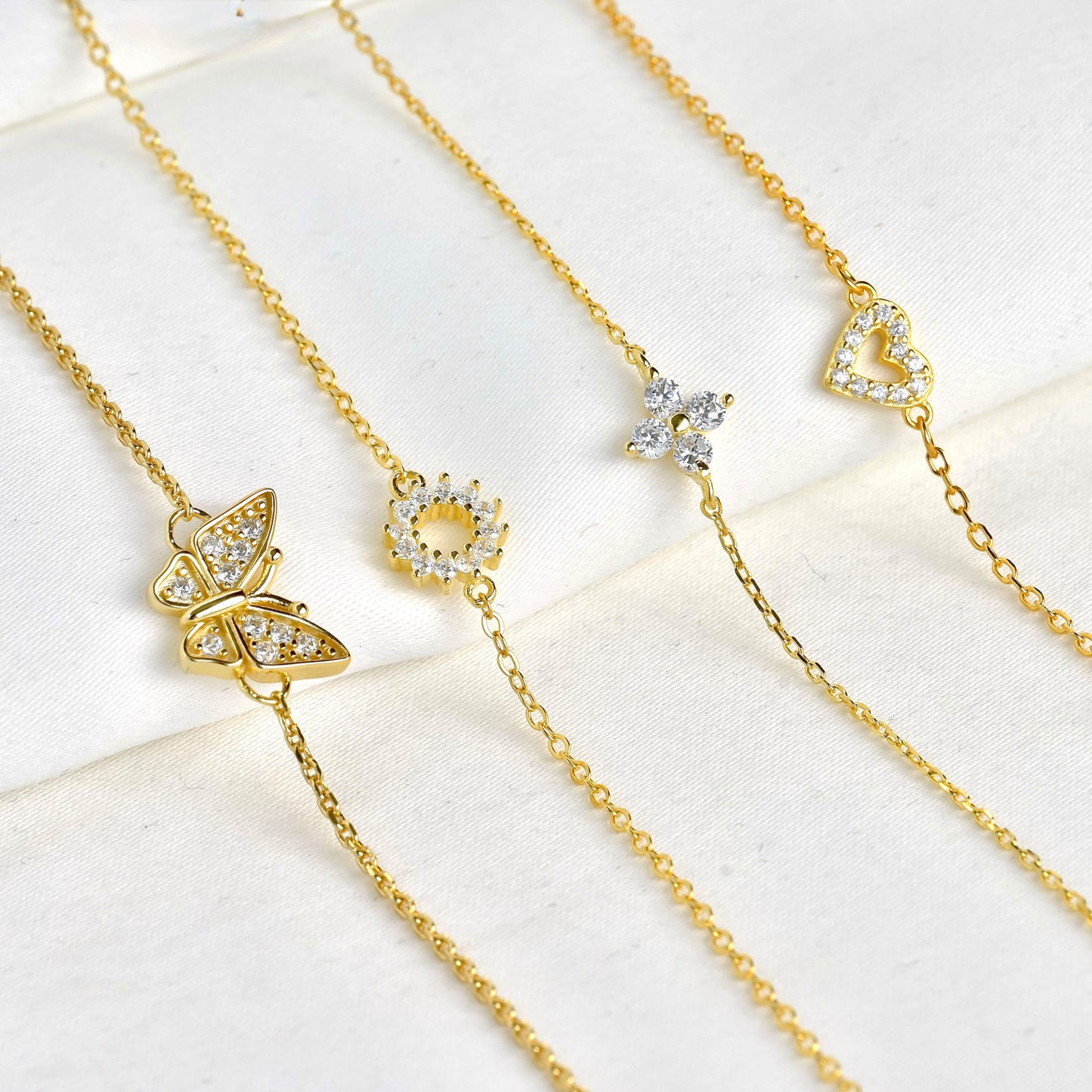 Four gold bracelets with pave diamond butterfly, sun, clover and heart charms on a white surface