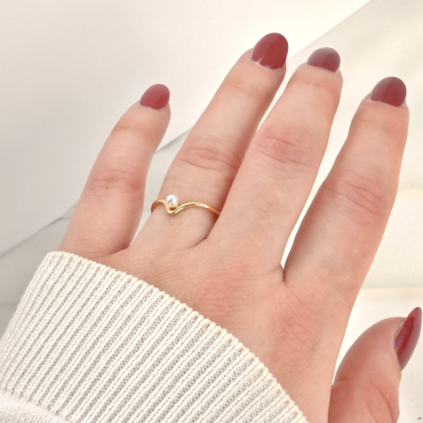Hand wearing a gold ring with a pearl on a light background