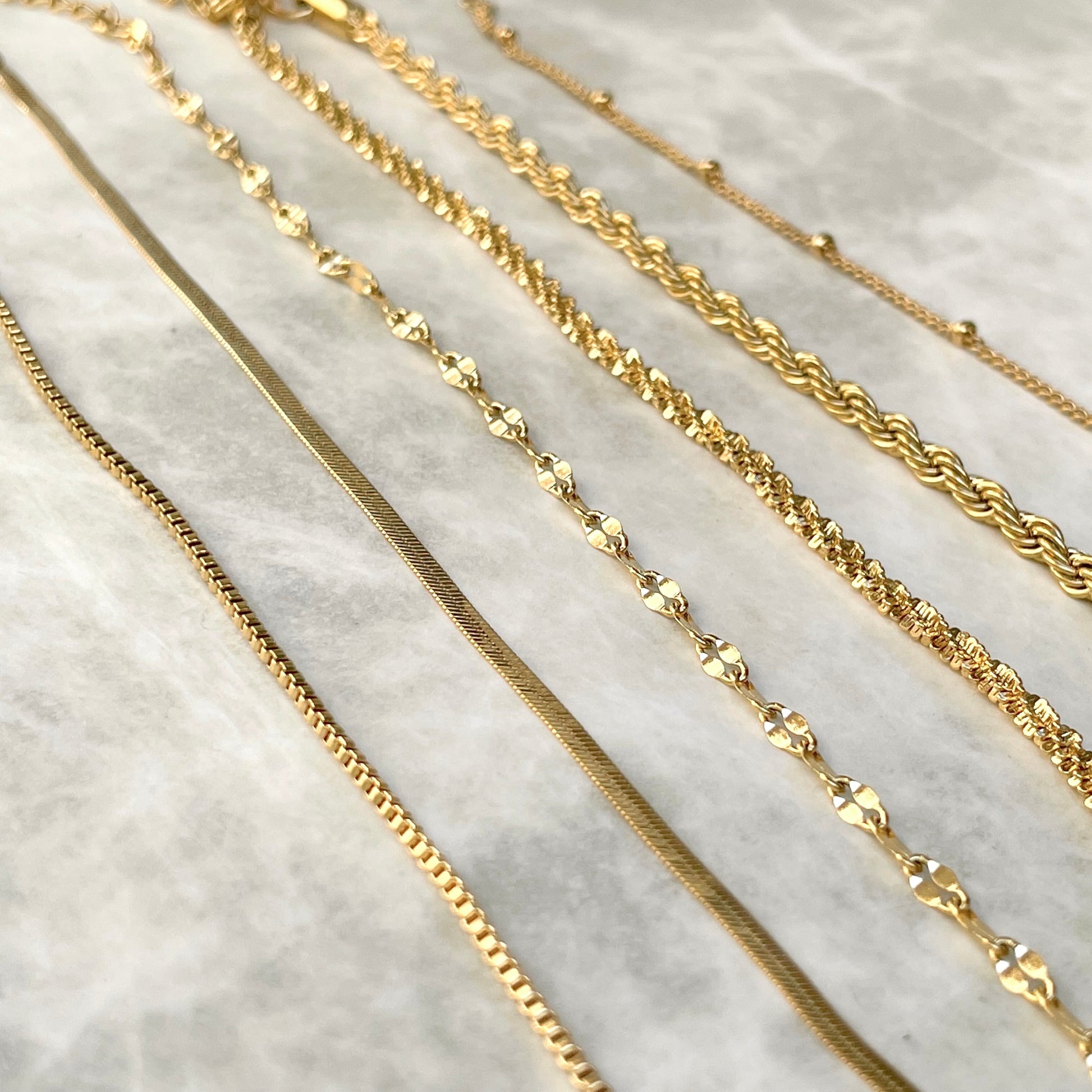 Angled view of gold bracelet chains of various designs on a marble surface