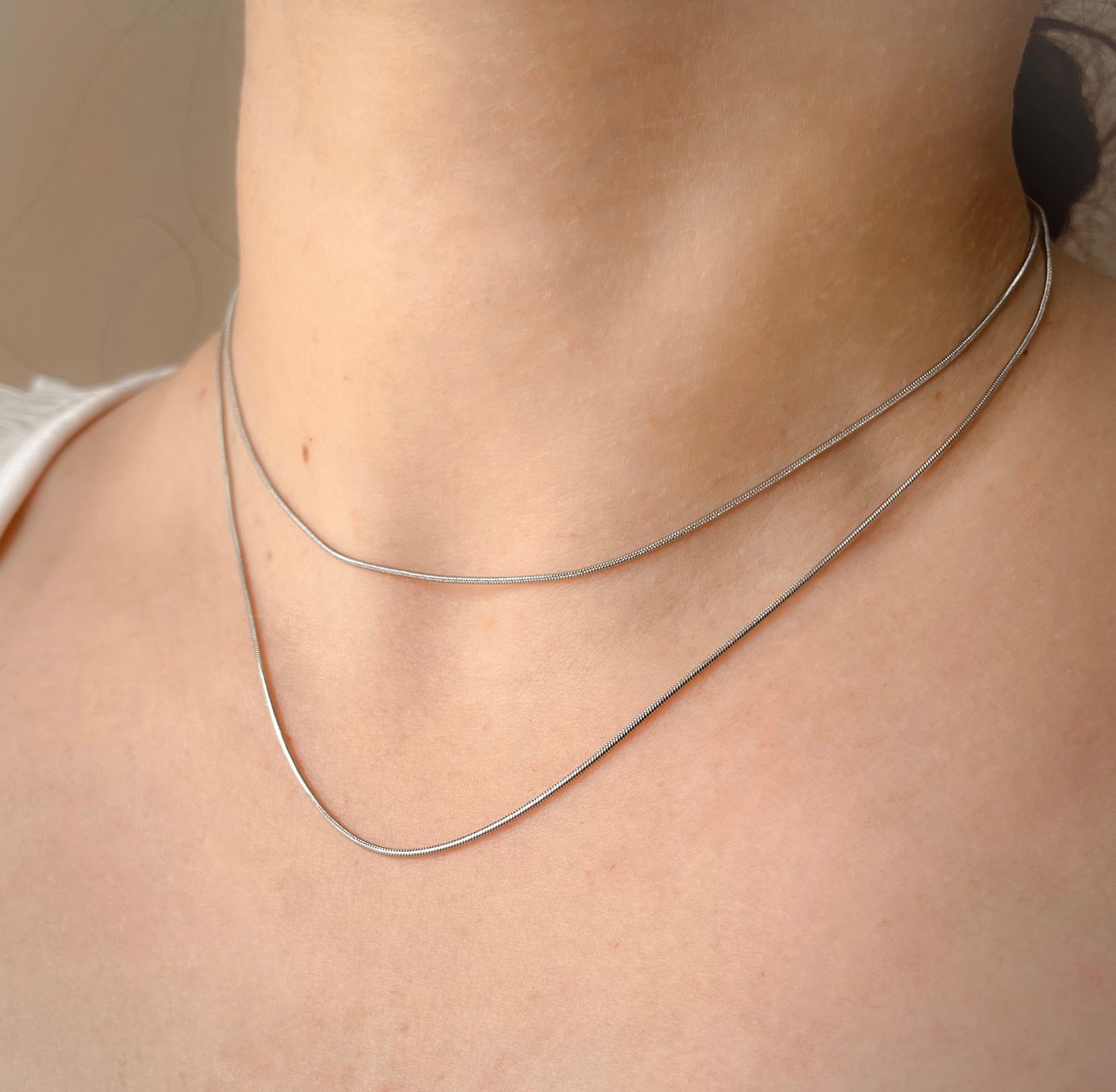 Double strand snake chain necklace on a person's neck against a neutral background