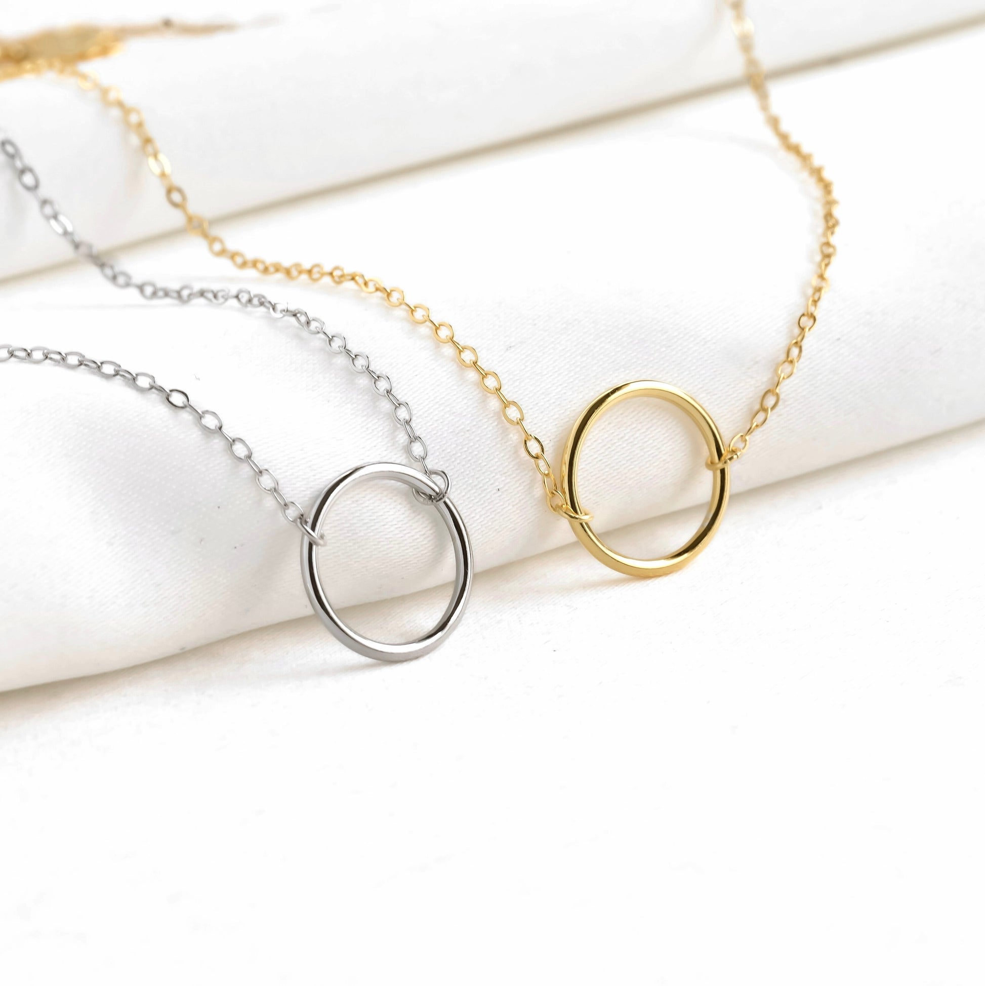 Two necklaces with circular pendants, one gold and one silver, on a white marble surface.