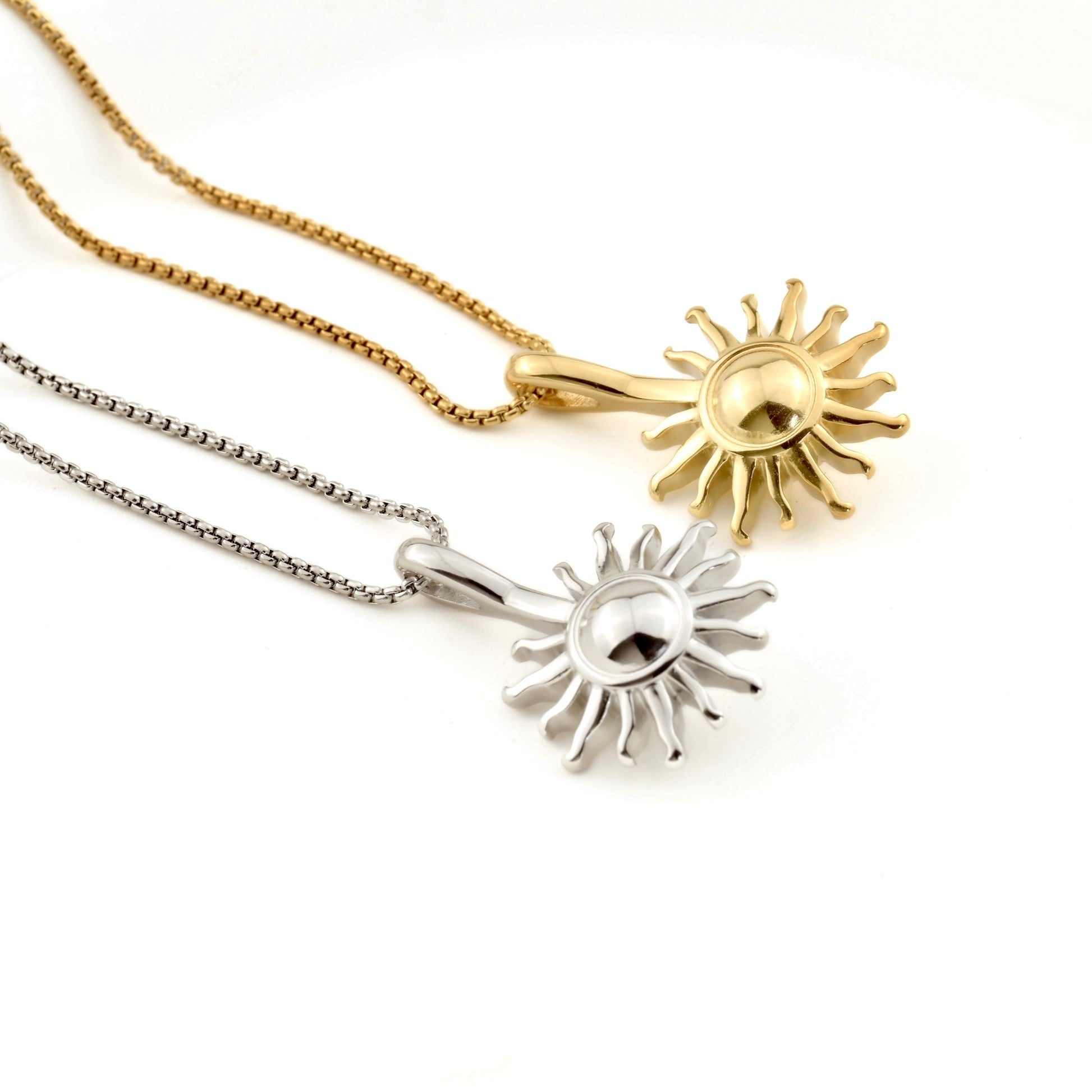 Two sun-shaped pendants, one gold and one silver, on white background