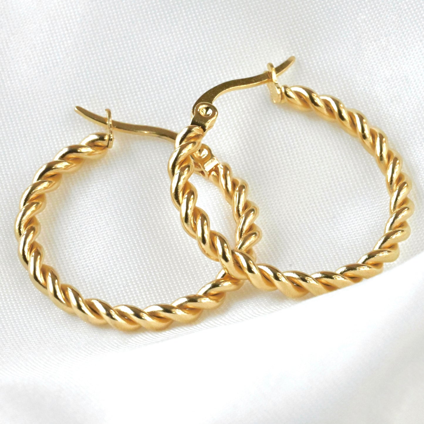 Close up view of gold rope hoop earrings with twisted design on a white background