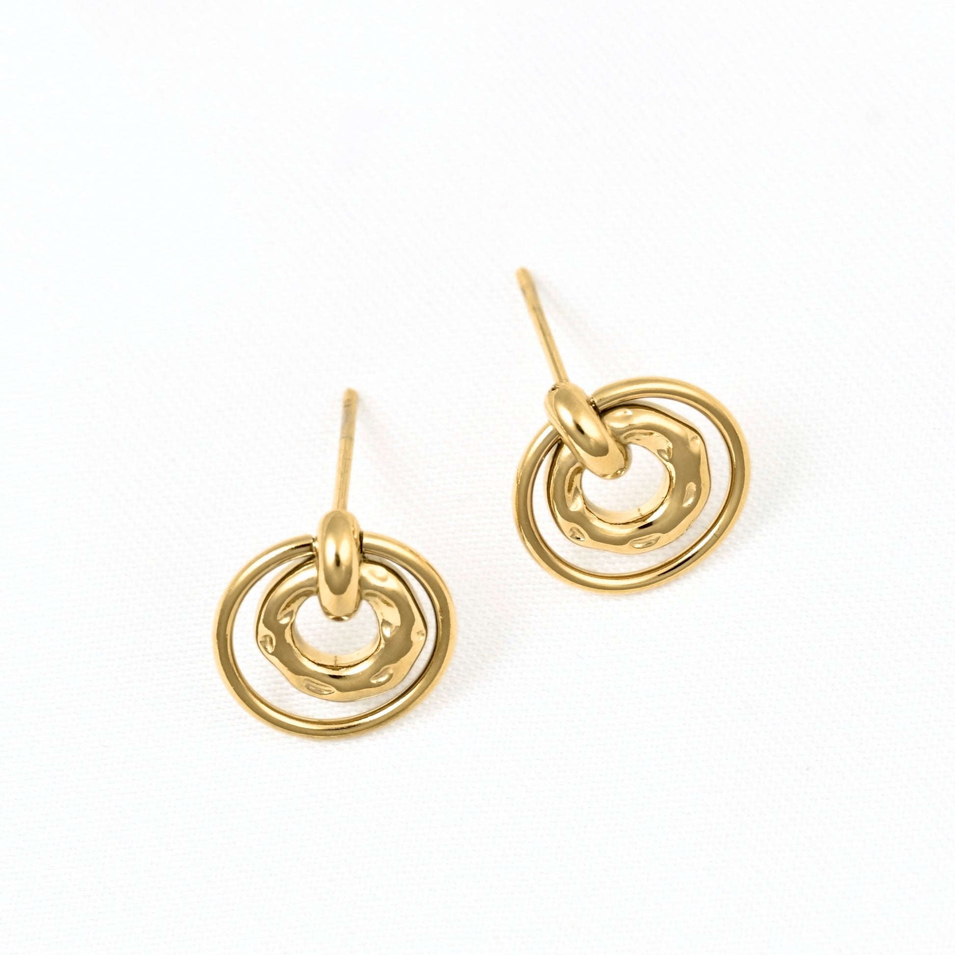 A pair of gold-toned stud earrings with a textured, hammered finish and concentric circular designs, shown on a clean white background.
