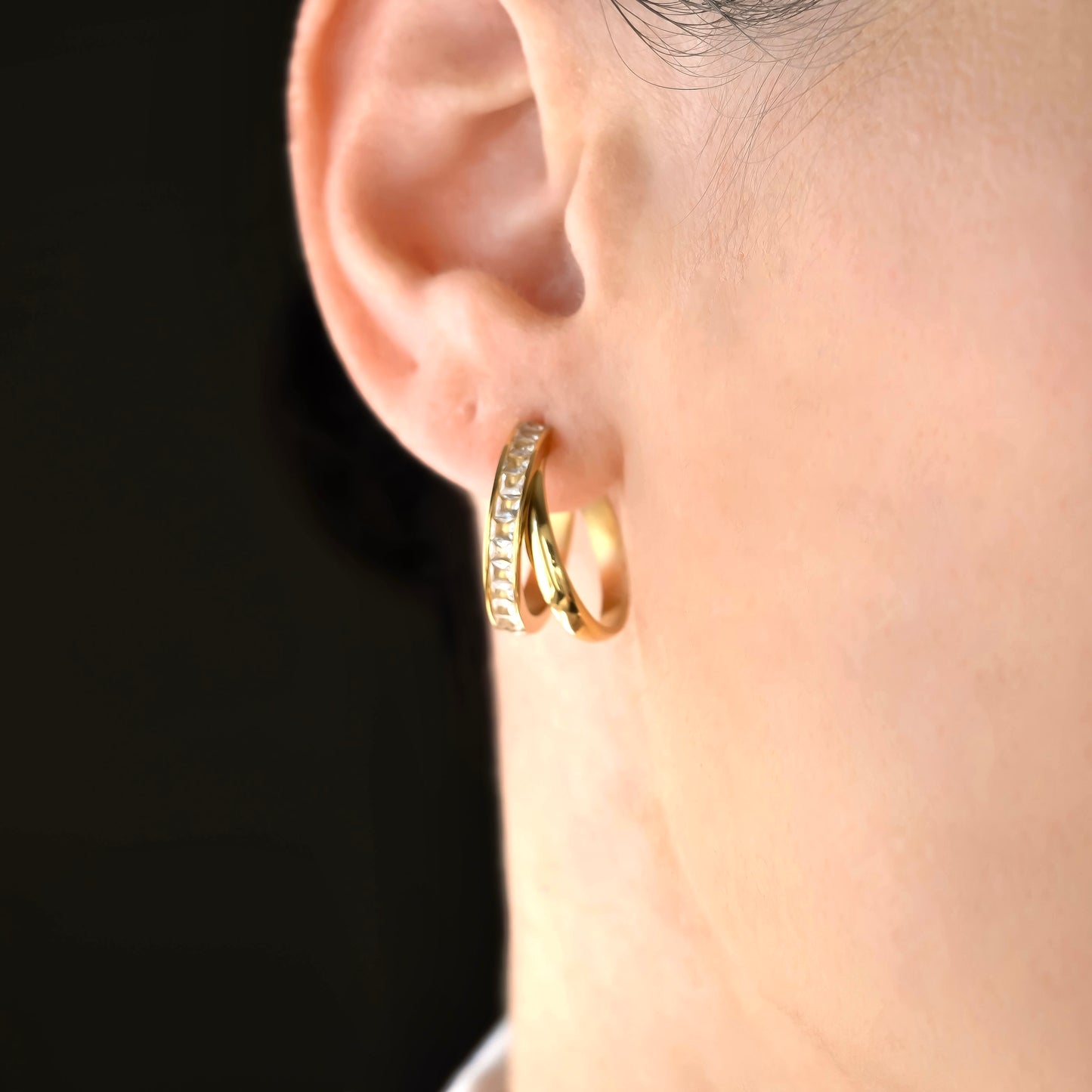 Close-up of a person wearing gold double hoop earrings with a blurred background