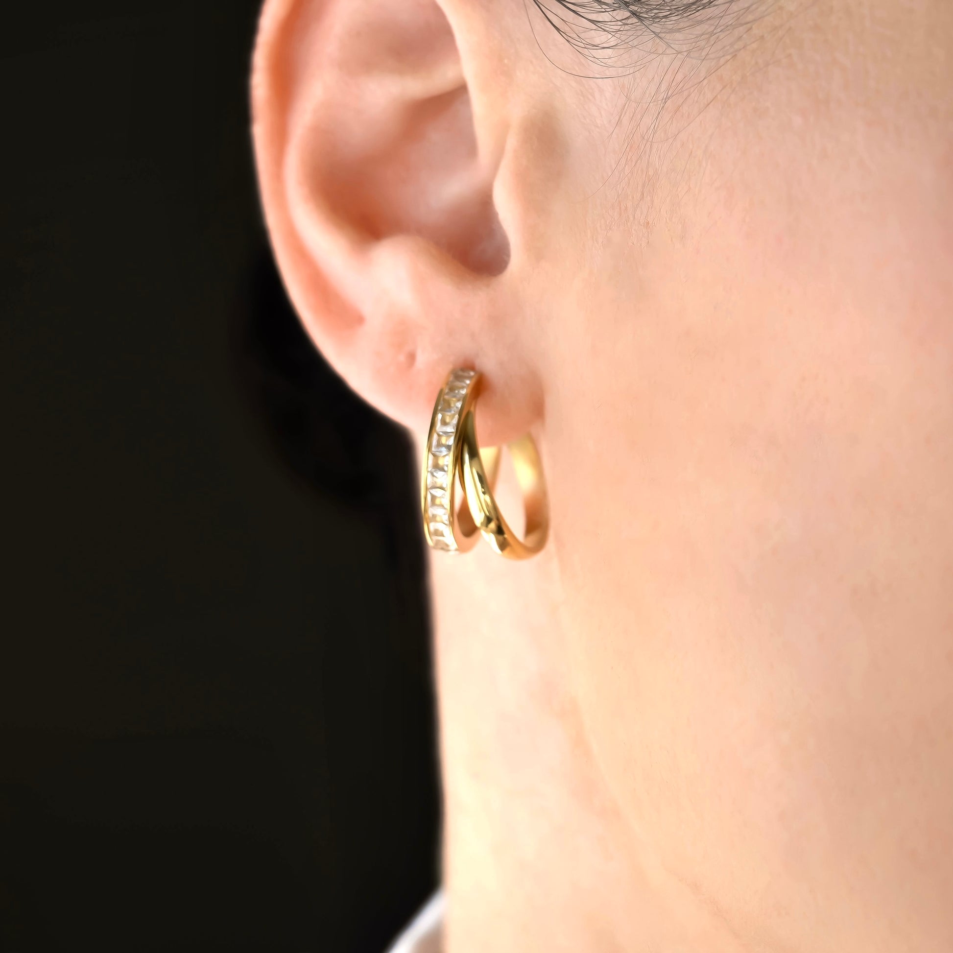 Close-up of a person wearing gold double hoop earrings with a blurred background