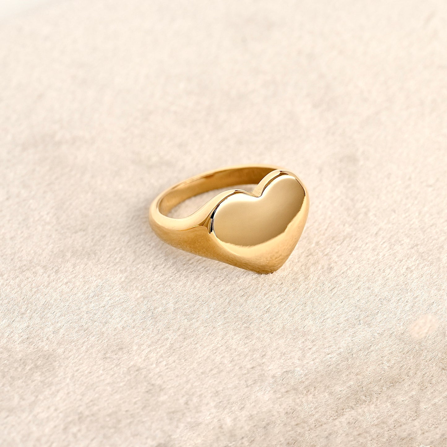 Oversized gold heart statement ring on a light beige background