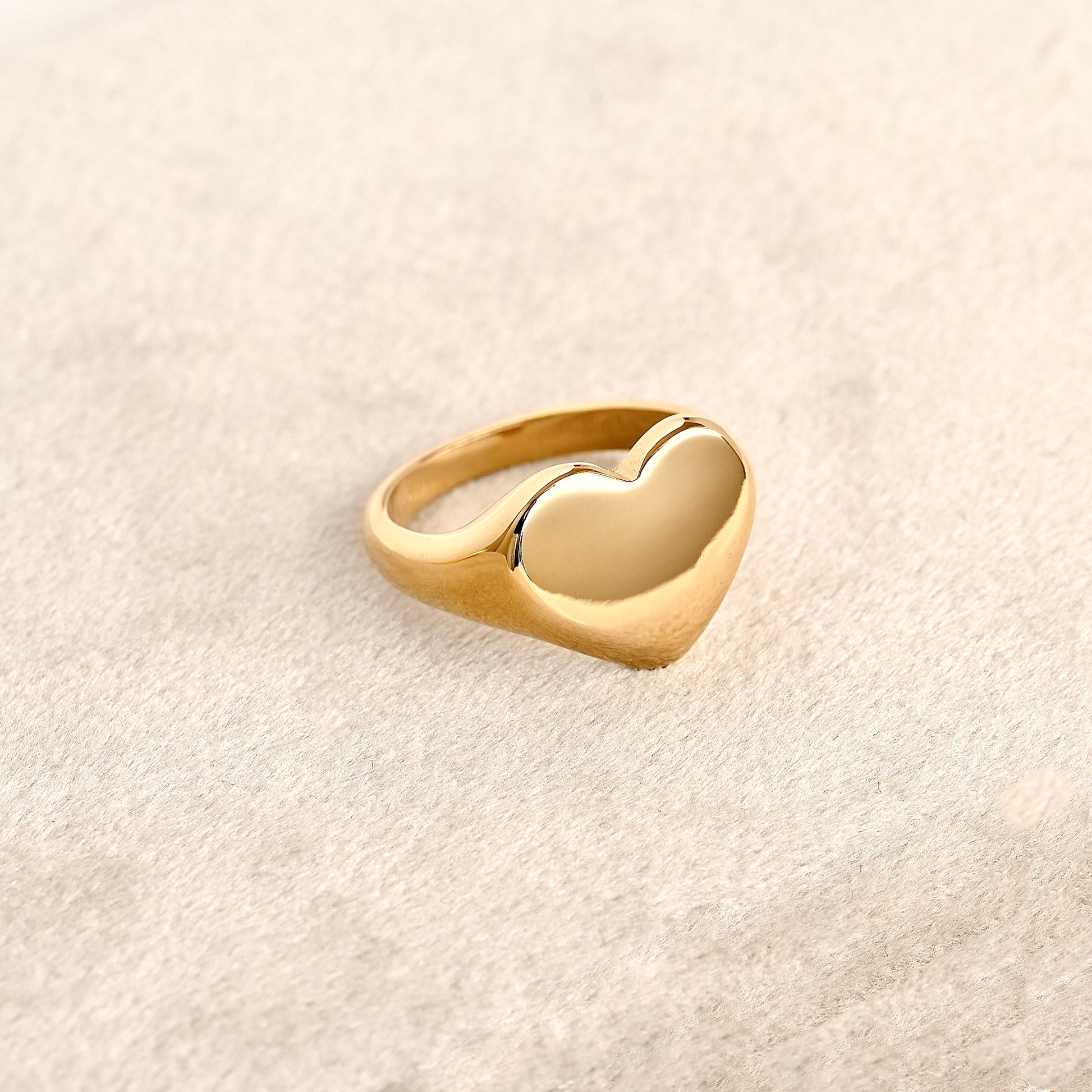 Oversized gold heart statement ring on a light beige background