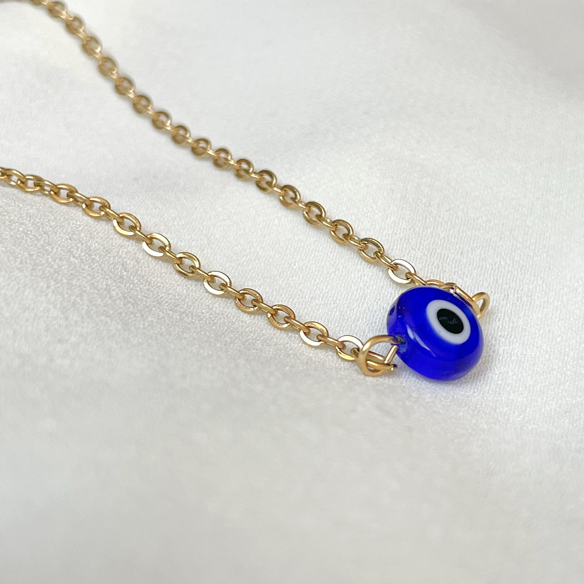 Side view of gold chain necklace with a round blue eye pendant on a white background