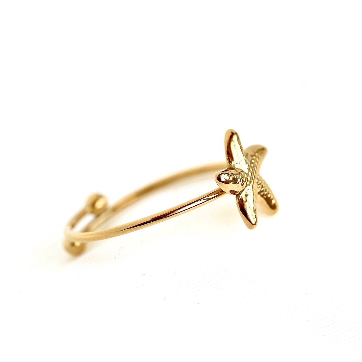 Side view of a gold-plated adjustable ring featuring a textured starfish charm, photographed on a seamless white background.