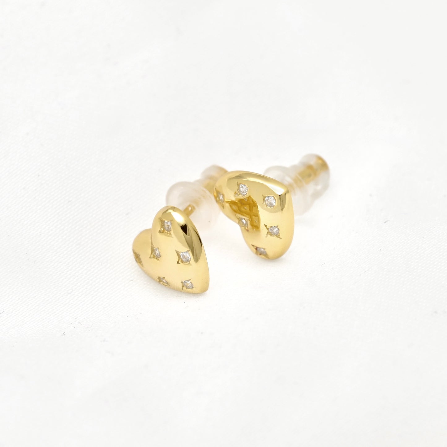 A pair of gold heart-shaped stud earrings with small clear gemstones and silicone backings, shown on a clean white background.