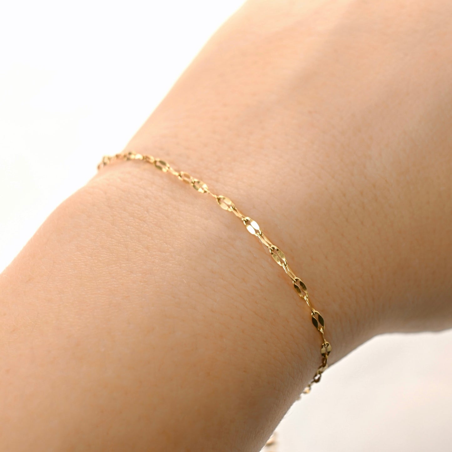 close up of a wrist wearing shimmering Gold chain against a white background