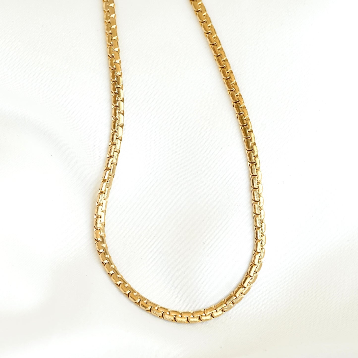 A gold-colored curb link chain necklace, shown draped in a U-shape against a plain white background.
