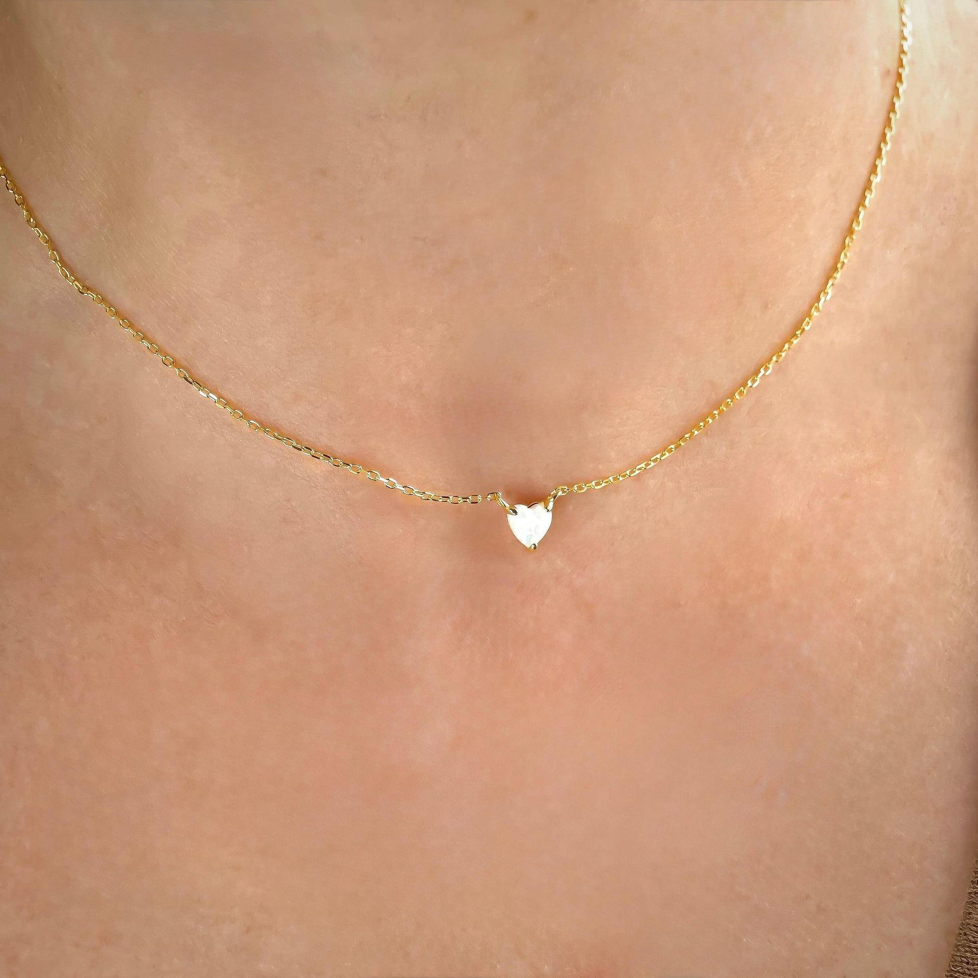 Gold necklace with an opal heart pendant on a person's neck